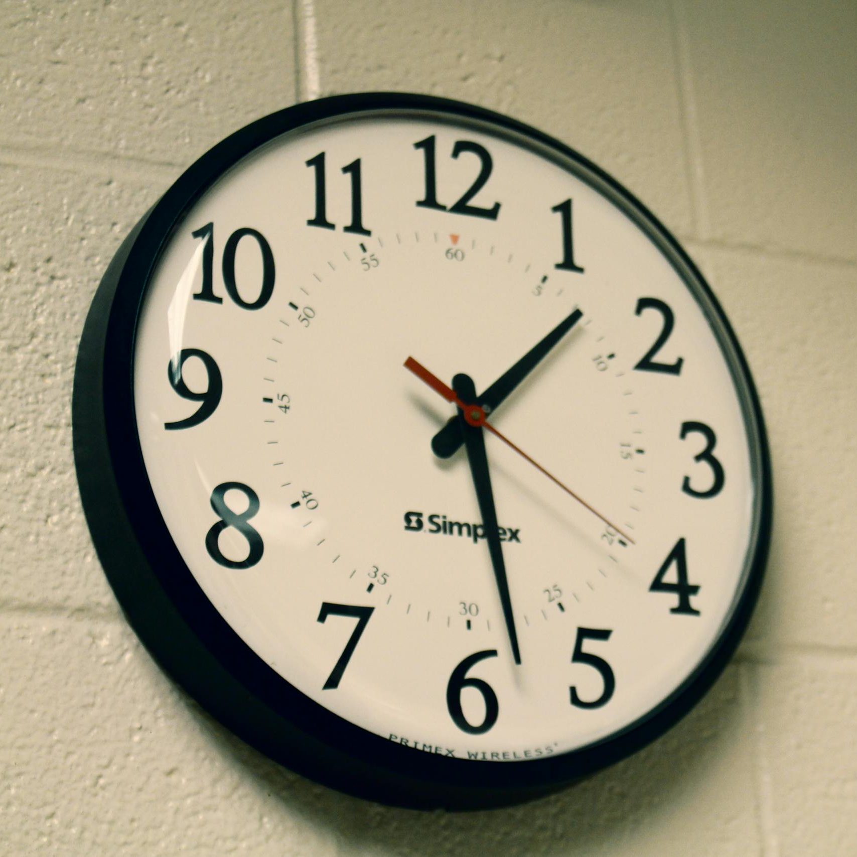 Simplex wall clock on a white brick wall, depicting time and simplicity.